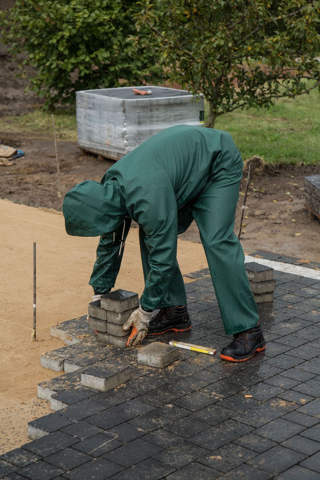 Worker in rain gear installing dark pavers on a construction site