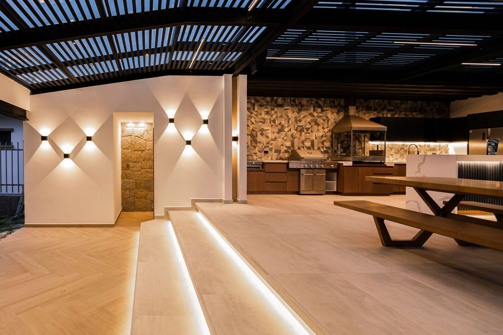 Covered outdoor kitchen with pergola roof, string lighting, and bar seating