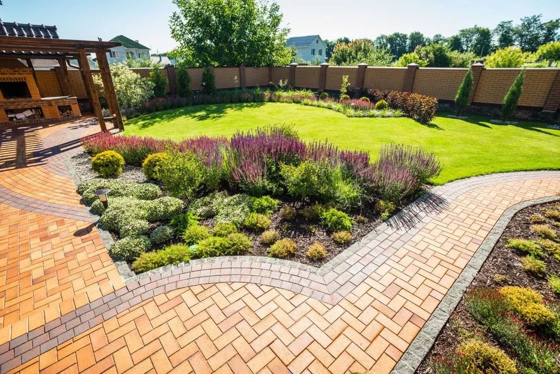 Herringbone brick patio bordering a circular lawn with planting beds and a pergola