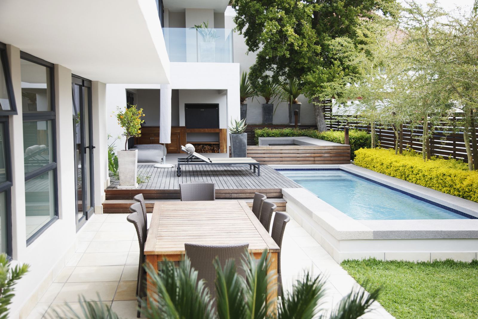 Modern backyard with a wood deck, dining table, and pool alongside a covered outdoor lounge area