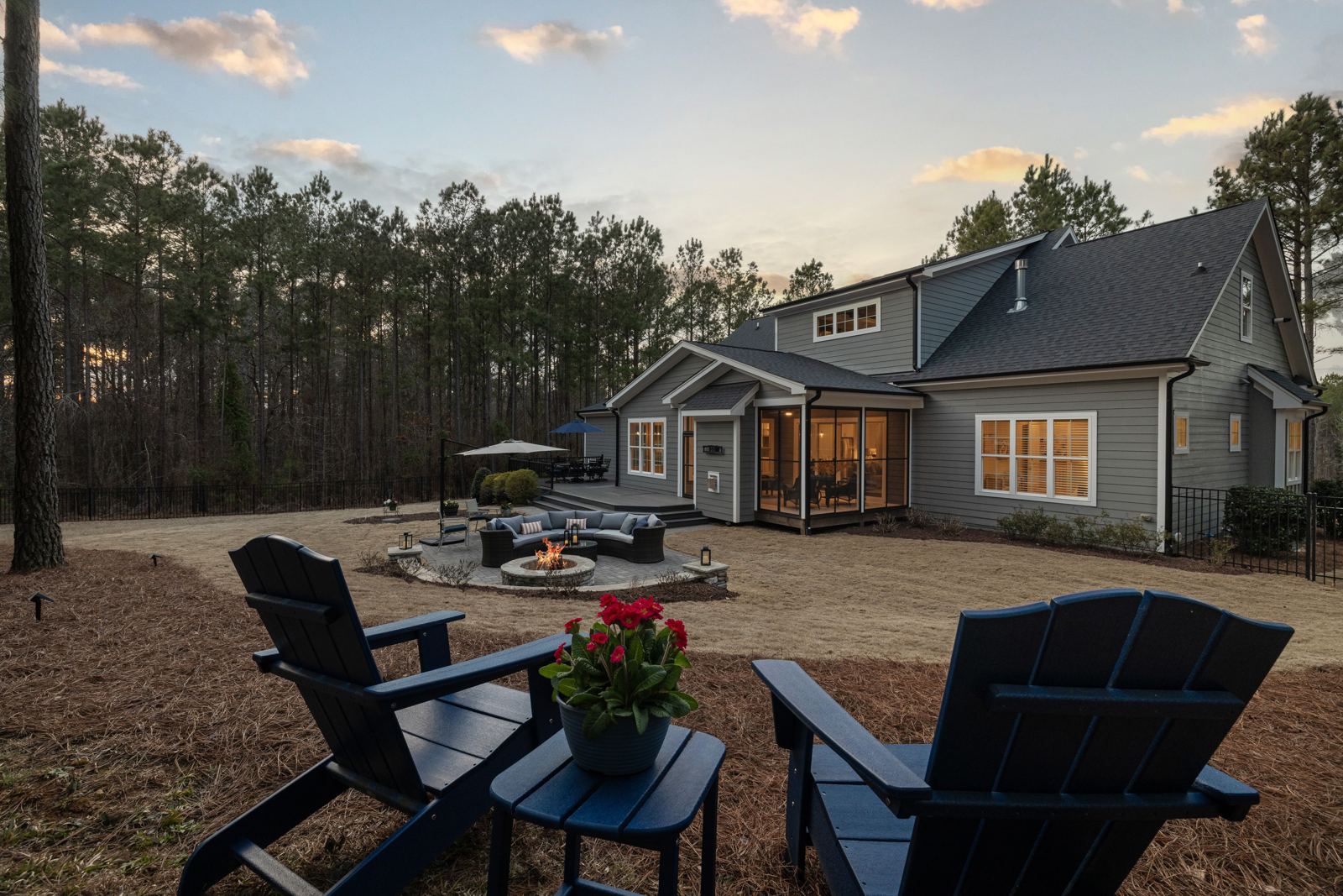 Backyard patio at dusk with a fire pit, seating area, and Adirondack chairs