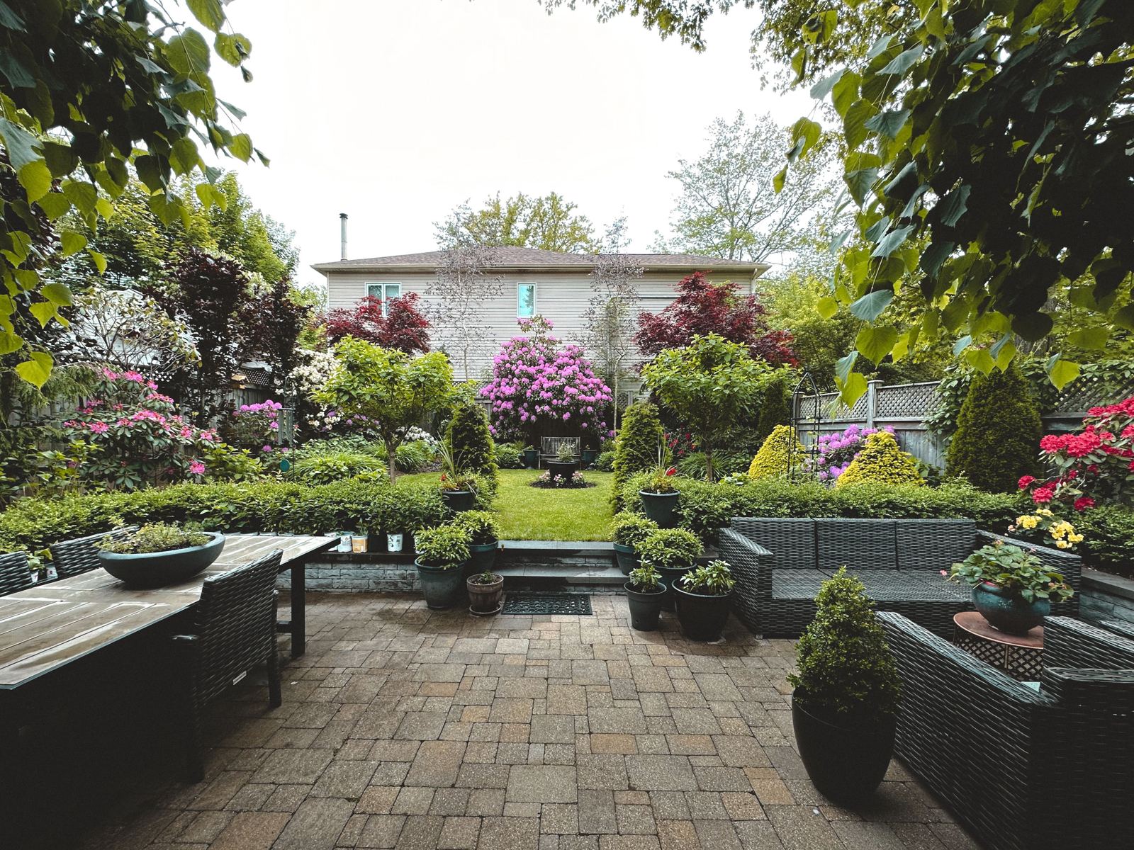 Backyard paver patio with pergola, dining table, and colorful garden beds