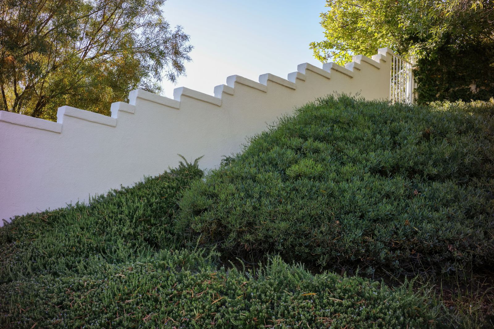 Tall white stone retaining wall terracing a sloped hillside with a cable railing above